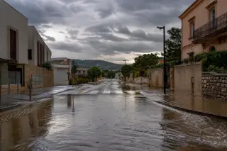 Flooded urban street in the Bouches-du-Rhône with cloudy sky, puddles reflecting buildings and hills in the background after intense autumn rain.